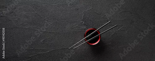 Obraz  z motywem Chopsticks and bowl with soy sauce on black stone background
