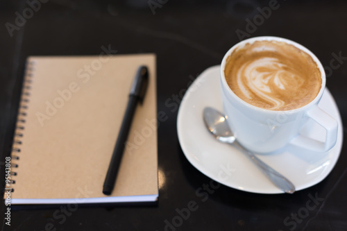 Hot latte art coffee cup on wooden table and note book.