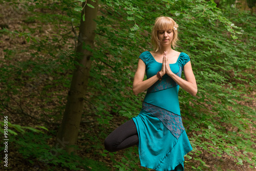 Young woman practicing yoga tree pose in forest.