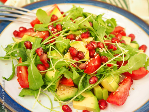 Salad with avocado slices, tomato wedges, sesame seeds, pomegranate seeds, rocket leaves and olive oil, closeup
