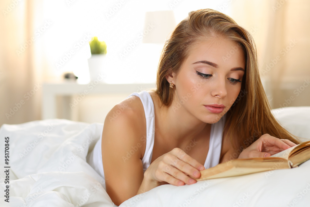 Young beautiful blonde woman lying in bed reading Young beautiful blonde woman lying in bed reading
