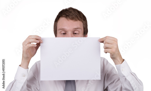 A caucasian male office worker holding a blank piece of paper in front of himself, looking down at the page where a message can be inserted. Isolated on white.