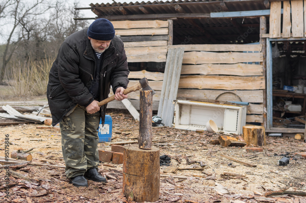 Old Ukrainian peasant choping firewood with an axe Old Ukrainian peasant choping firewood with an axe