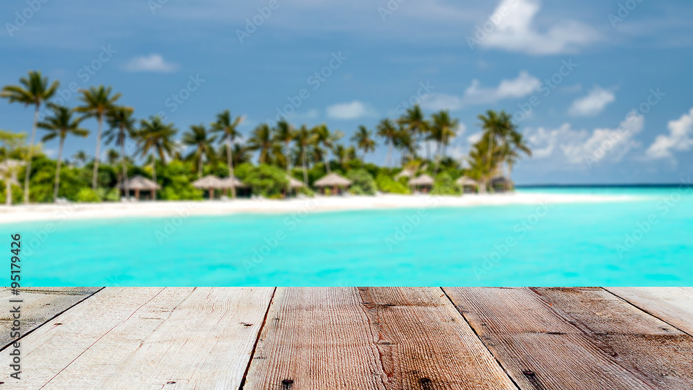 Fototapeta premium wooden front with tropical island blurred background, maldives island with palm trees and wooden bungalows
