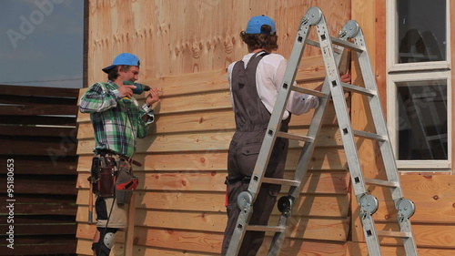Work on Installing Siding/Standing on a stairs, carpenter fixes the siding on the house