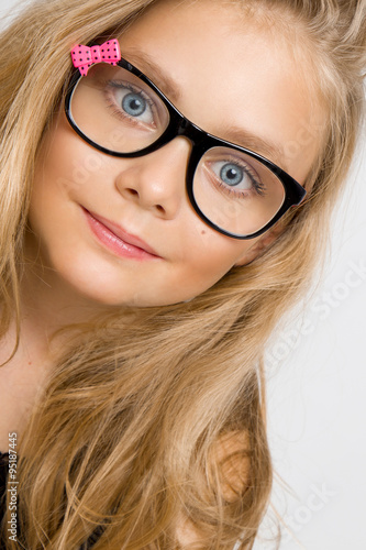 Portrait of a lovely little girl daughter in long blond hair and black glasses with pink bow which looks at the camera, photo on the white background ammazing eyes photo