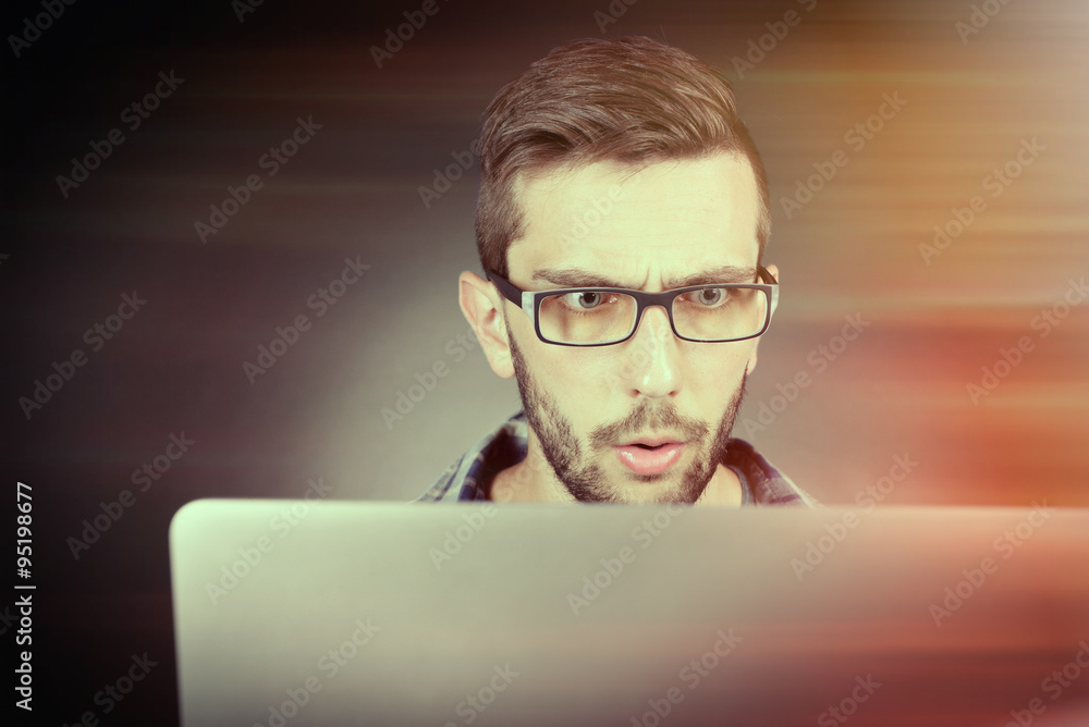 Handsome young man with laptop on dark background