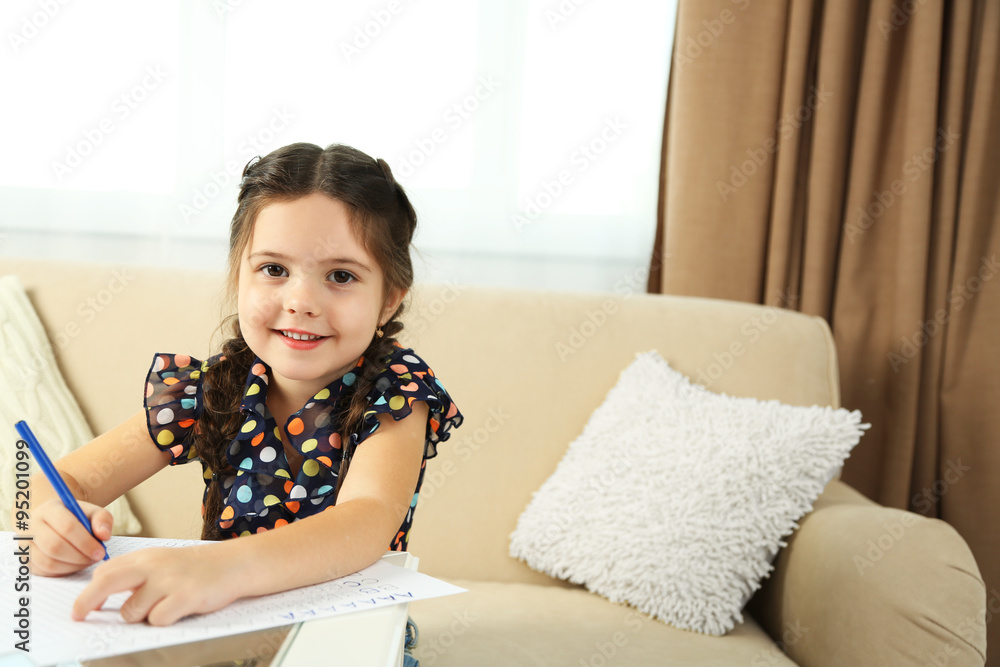 Cute little girl doing her homework, close-up, on home interior background Cute little girl doing her homework, close-up, on home interior background