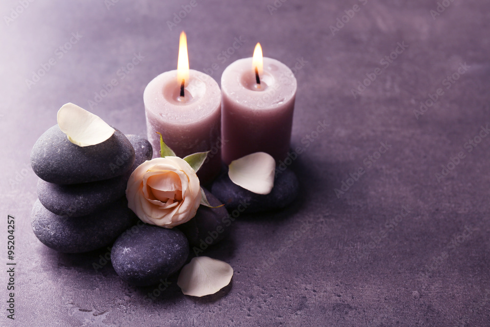 Relax concept - composition of aroma candles with pebbles and flower on grey background Relax concept - composition of aroma candles with pebbles and flower on grey background