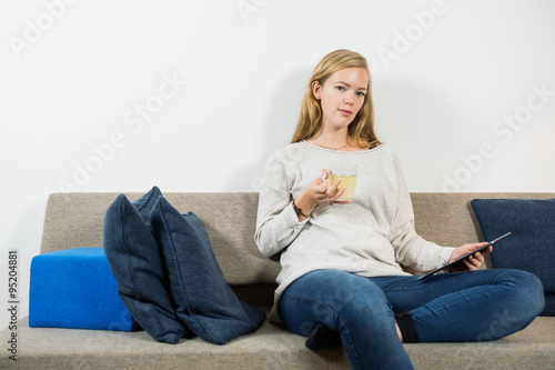 Woman Holding Drink And Digital Tablet On Sofa