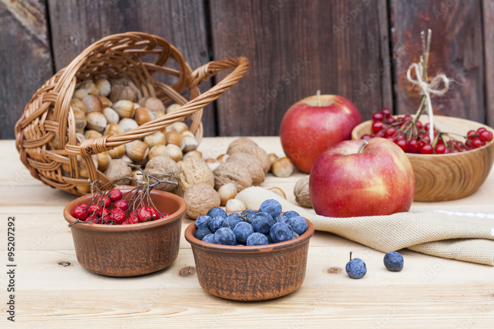 Autumn still life with walnuts and hazelnuts in the basket and autumn berry and vegetables on old wooden background, closeup Autumn still life with walnuts and hazelnuts in the basket and autumn berry and vegetables on old wooden background, closeup