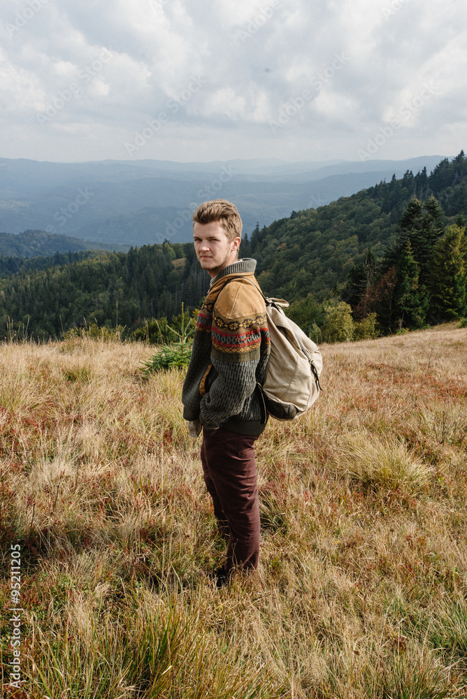 stylish beautiful traveling man hiking in the mountains on a bac