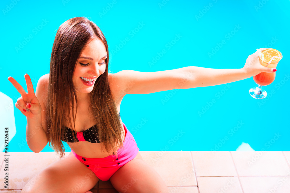 Woman with cocktail drink at swimming pool edge.