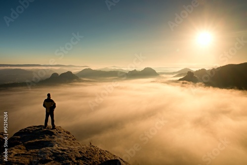 Fotografie Man stands on peak of sandstone rock in Saxony Switzerland park and watching to Sun