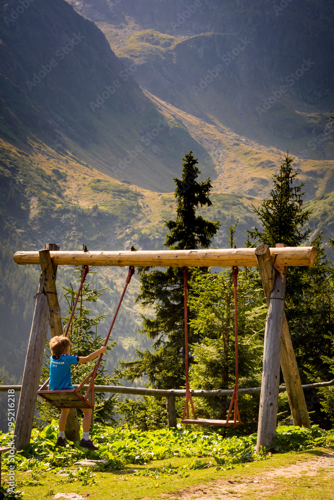 A little boy is swinging on a swing in the mountains A little boy is swinging on a swing in the mountains