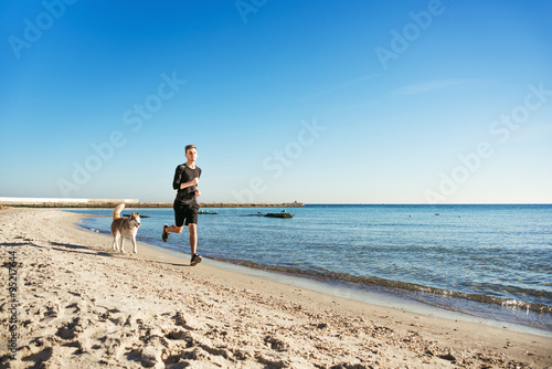 Running man. Male runner jogging with siberian husky dogs during the sunrise on beach
