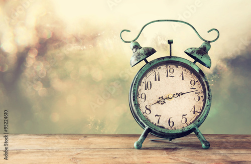 image of vintage alarm clock on wooden table in front of abstract blurred background. retro filtered 
