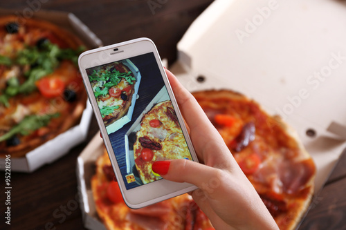 Woman taking a photo of pizza with the smartphone photo