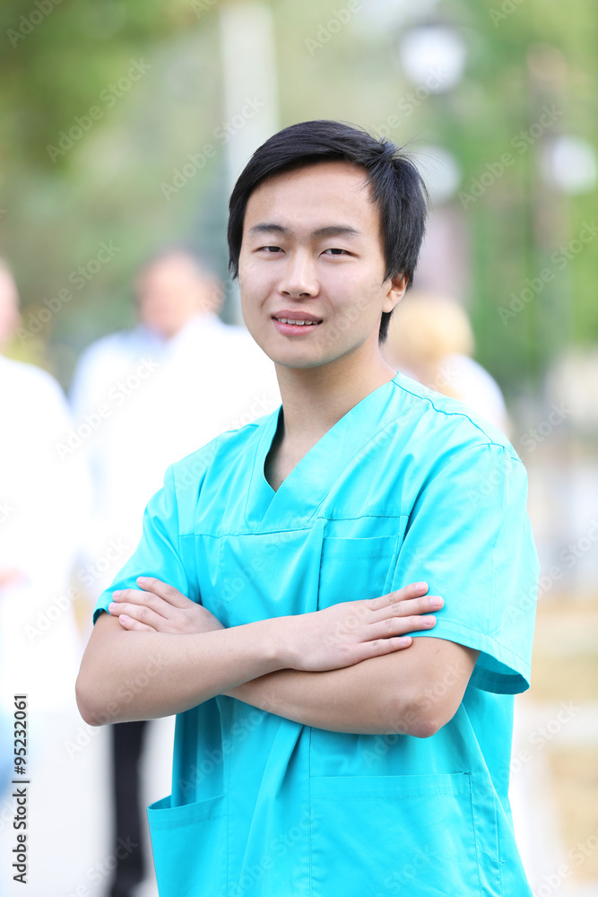 Young smiling doctor standing against unfocused group of medical workers Young smiling doctor standing against unfocused group of medical workers