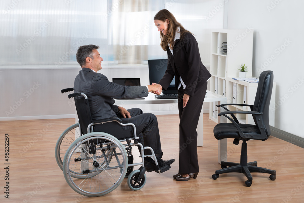 Businesswoman Shaking Hands With Businessman On Wheelchair Businesswoman Shaking Hands With Businessman On Wheelchair