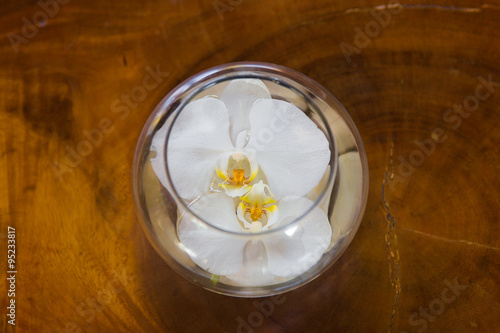 White orchid flower in glass vase with water on wooden backgroun