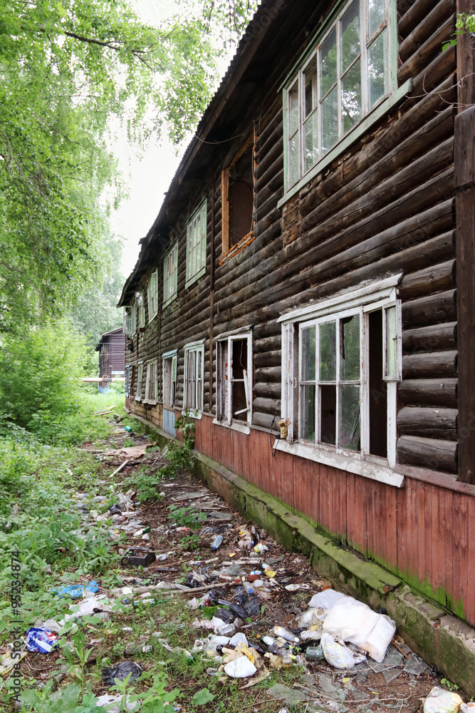 Old wooden two-story abandoned building with garbage in summer