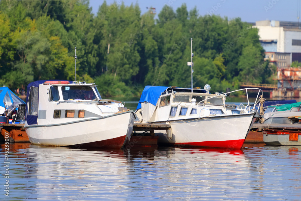 Small modern motorboats at pier on river at summer sunny day Small modern motorboats at pier on river at summer sunny day