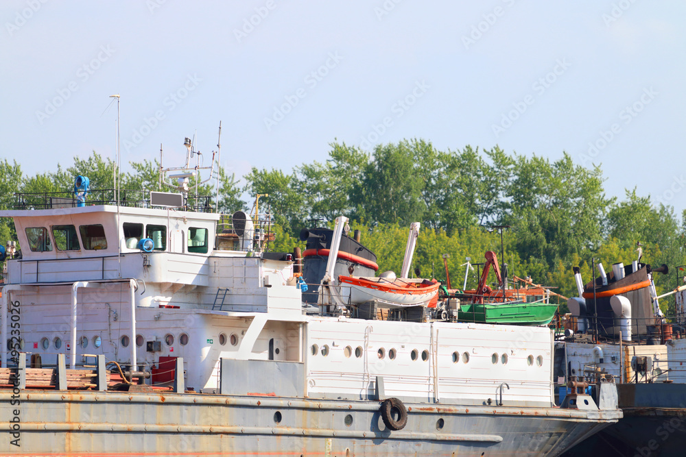 Fototapeta premium Parts of rusty cargo ships with lifeboats on river at summer 
