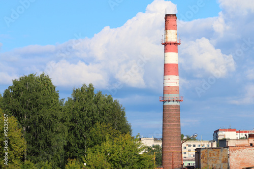 Tall chimney pipe of modern plant among green trees in city 