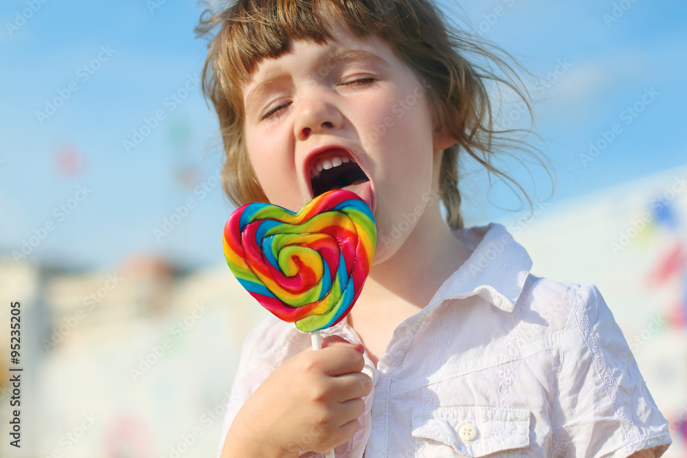 Happy little girl licks bright lollipop outdoor in town Happy little girl licks bright lollipop outdoor in town