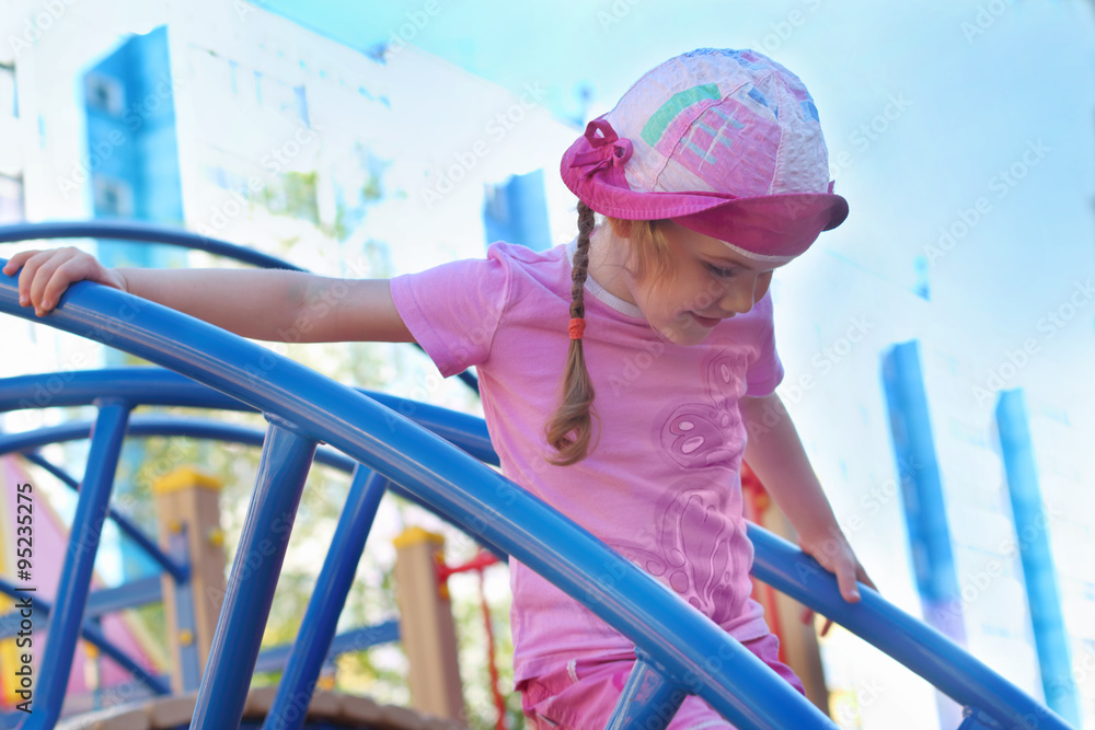Pretty little girl plays on wooden children playground at summer