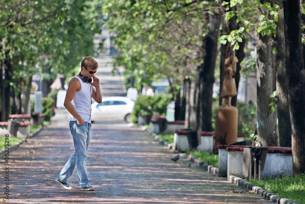 Man in sunglasses walks on alley with green trees and benches Man in sunglasses walks on alley with green trees and benches