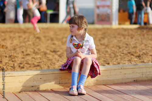 Happy little girl sits with bright lollipop and looks away 