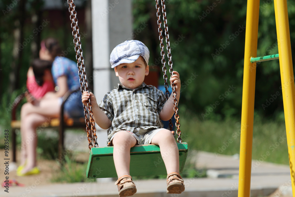 Handsome little boy in cap swings on children playground Handsome little boy in cap swings on children playground