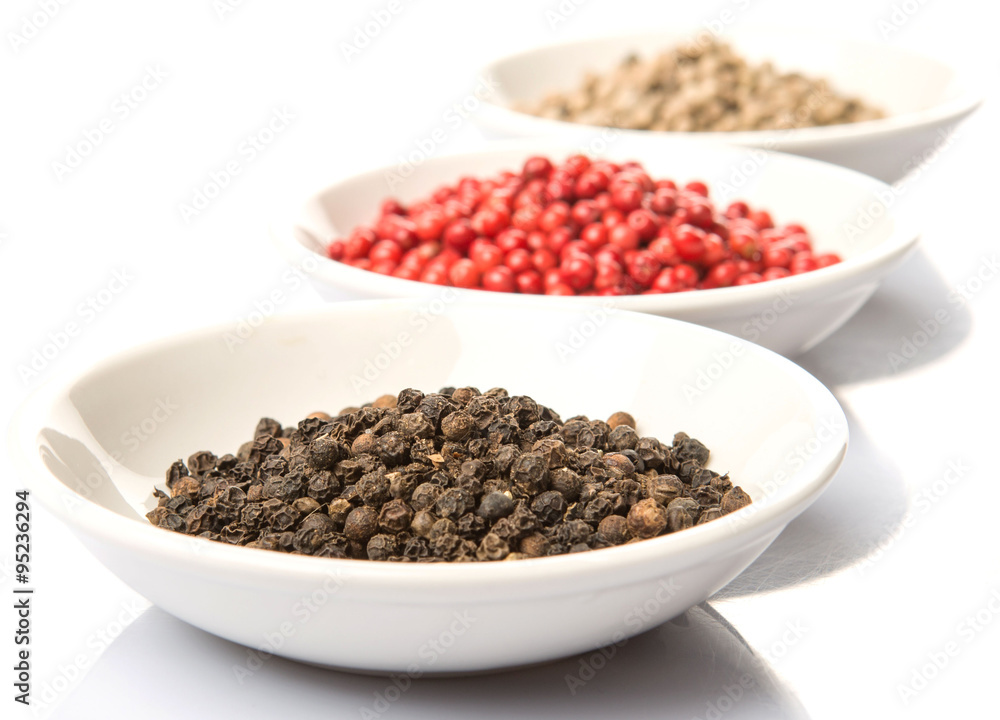 Black, white and pink peppercorn in white bowl over white background Black, white and pink peppercorn in white bowl over white background