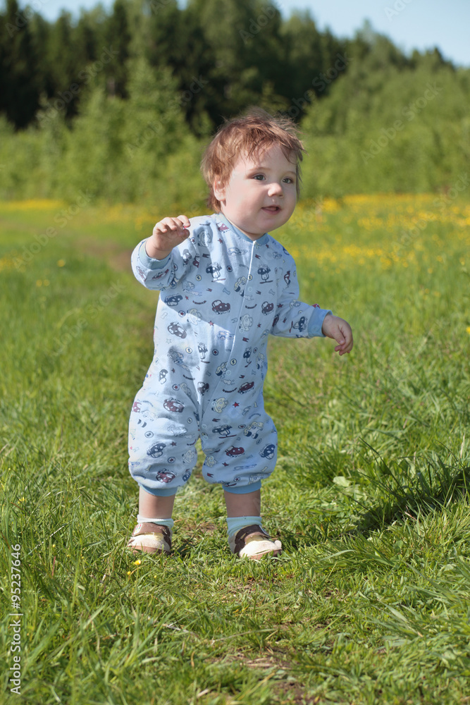 Happy little cute baby stands on green grass near forest Happy little cute baby stands on green grass near forest