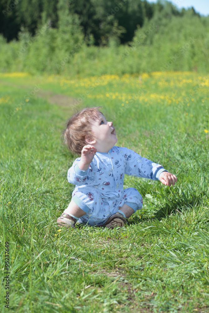 Happy little cute baby sits on green grass near forest Happy little cute baby sits on green grass near forest