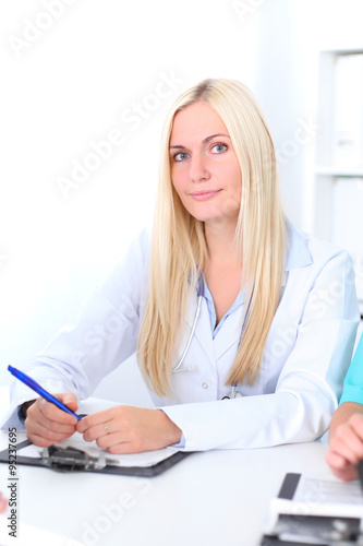 Two confident friendly female doctors sitting at the table and listen to the patient s history . Fokus on blonde female doctor. Medical and health care concept