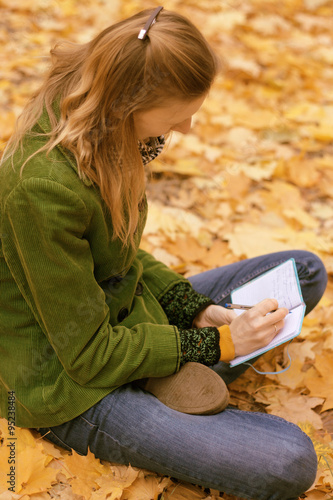 Girl in autumn leaves with a notebook