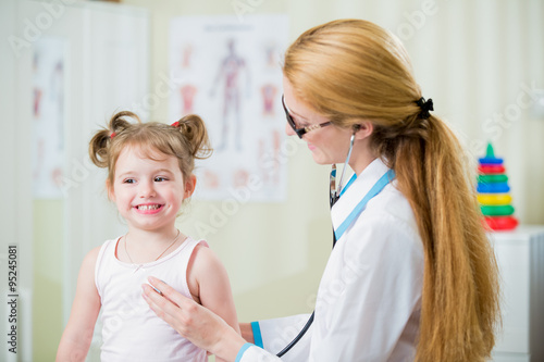 Pediatrician woman examining cute little girl with stethoscope. Kid happily smiling