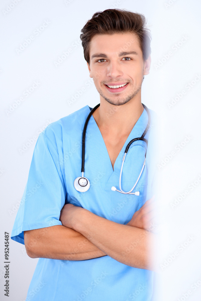 Attractive male doctor standing near the wall, crossed arms Attractive male doctor standing near the wall, crossed arms