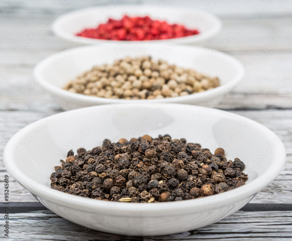 Black, white and pink peppercorn in white bowl over wooden background Black, white and pink peppercorn in white bowl over wooden background