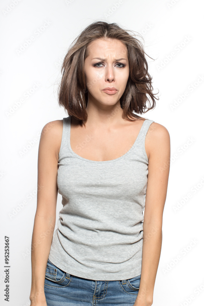 Awesome Caucasian attractive sexy female model with brunette hair is grimacing in studio, wearing grey sleeveless shirt and jeans, isolated on white background Awesome Caucasian attractive sexy female model with brunette hair is grimacing in studio, wearing grey sleeveless shirt and jeans, isolated on white background