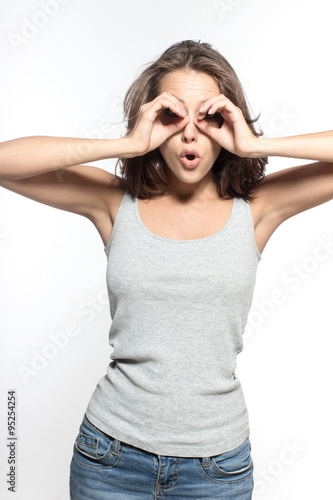 Awesome Caucasian attractive sexy female model with brunette hair is grimacing in studio, wearing grey sleeveless shirt and jeans, isolated on white background
