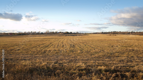 Country landscape with a field and a village tucked away in the background on a bright sunny autumn day in the afternoon