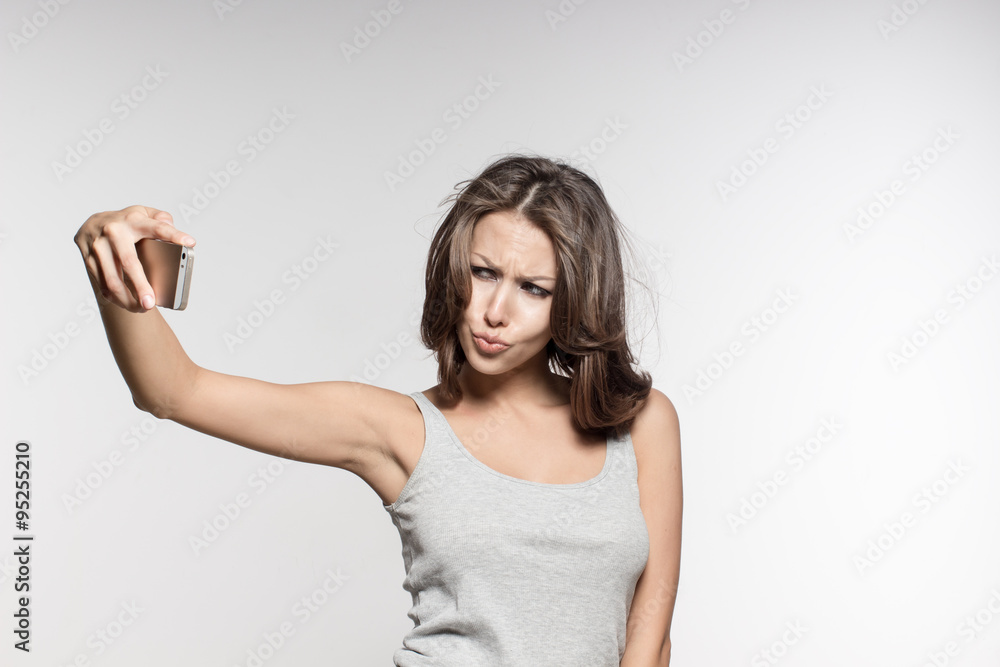 Fototapeta premium attractive female model is grimacing, making selfies, grey shirt and jeans, white background
