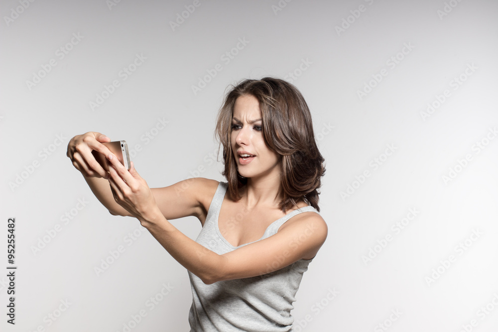 attractive female model is grimacing, making selfies, grey shirt and jeans, white background attractive female model is grimacing, making selfies, grey shirt and jeans, white background