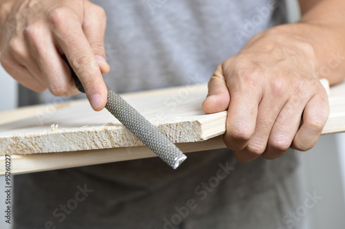 young man filing a wooden board with a rasp photo