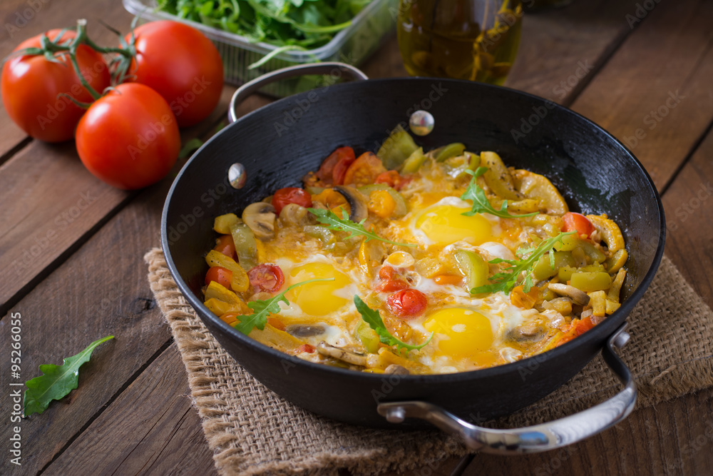 Fried eggs with vegetables in a frying pan on a wooden background Fried eggs with vegetables in a frying pan on a wooden background