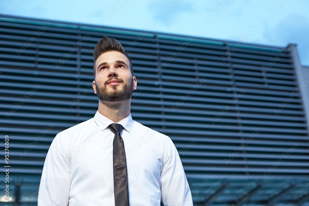 Businessman in front of business building smiling and looking co Businessman in front of business building smiling and looking co
